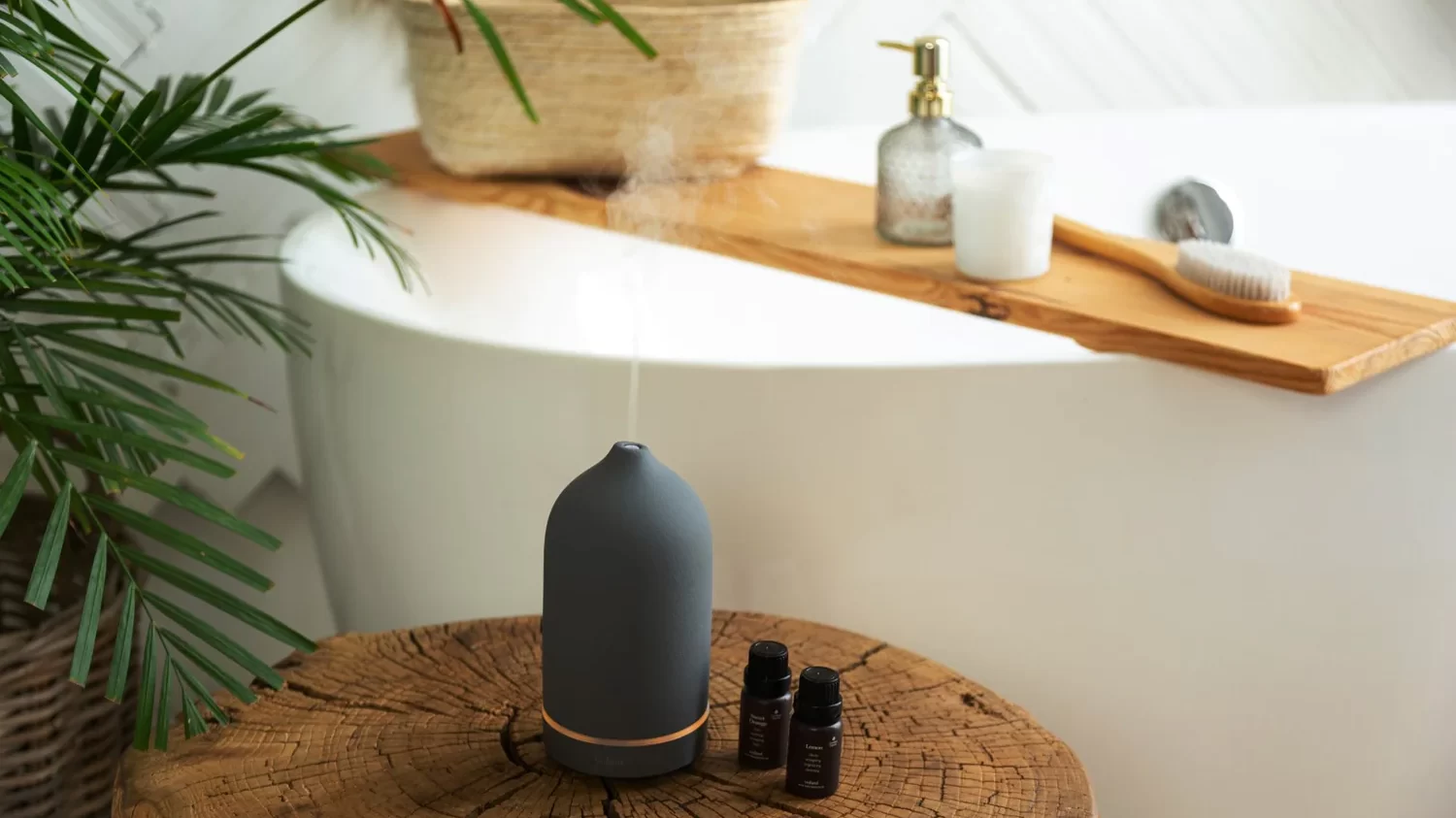 Aromatherapy diffuser releasing steam beside a freestanding bathtub with wooden bath tray and spa accessories